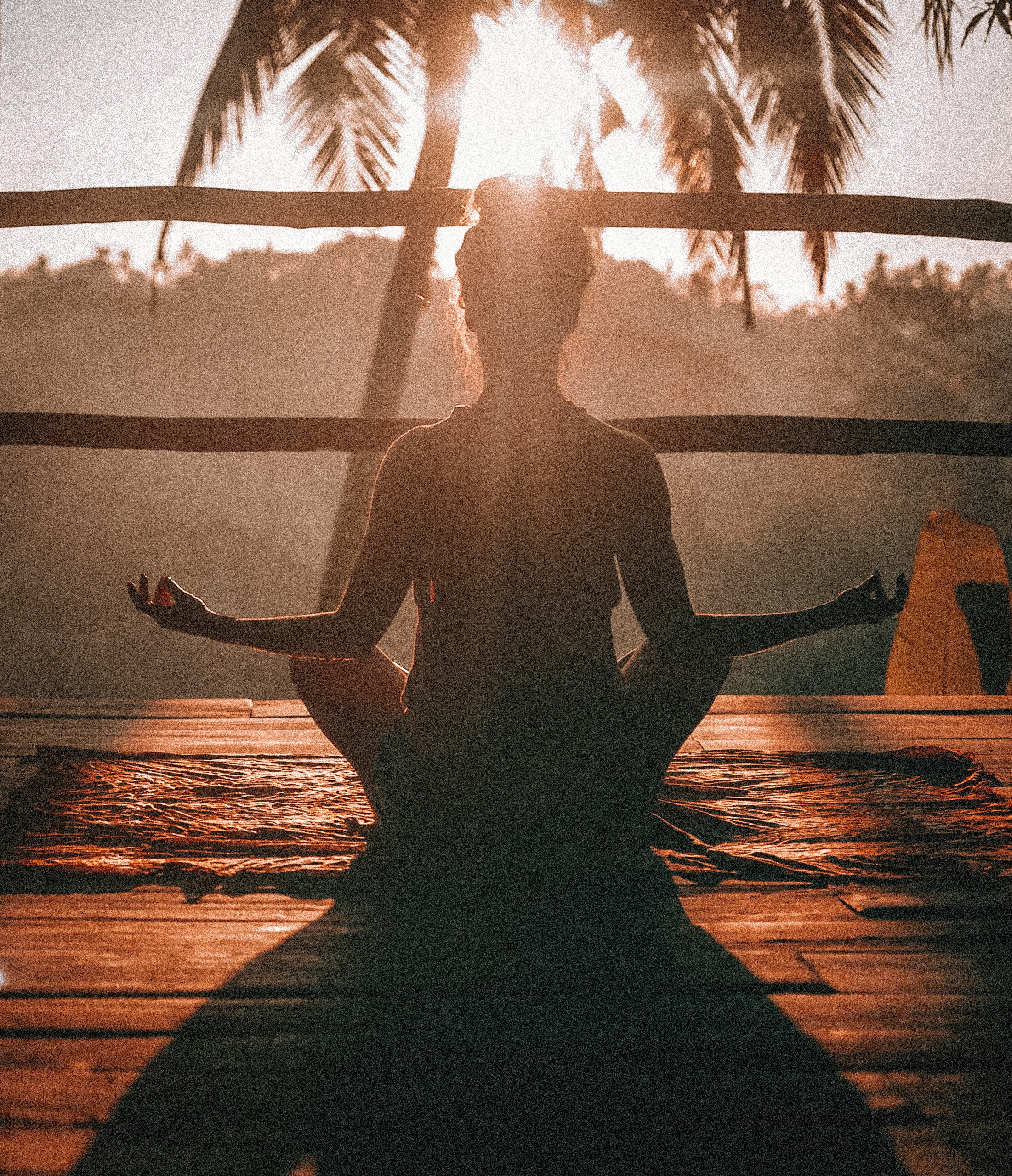 Une jeune femme est en position du Lotus face au soleil. Elle est à contre-jour.